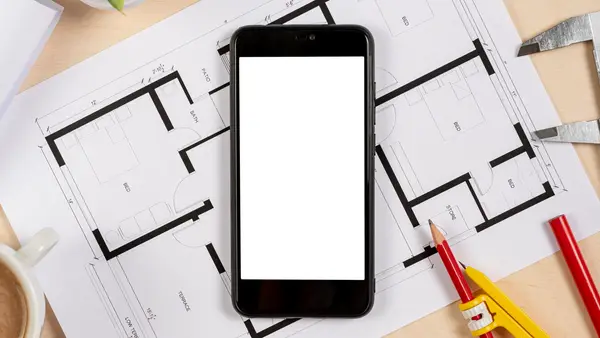 A smartphone resting on architectural plans with measuring tools, representing how a clear app specification determines development cost