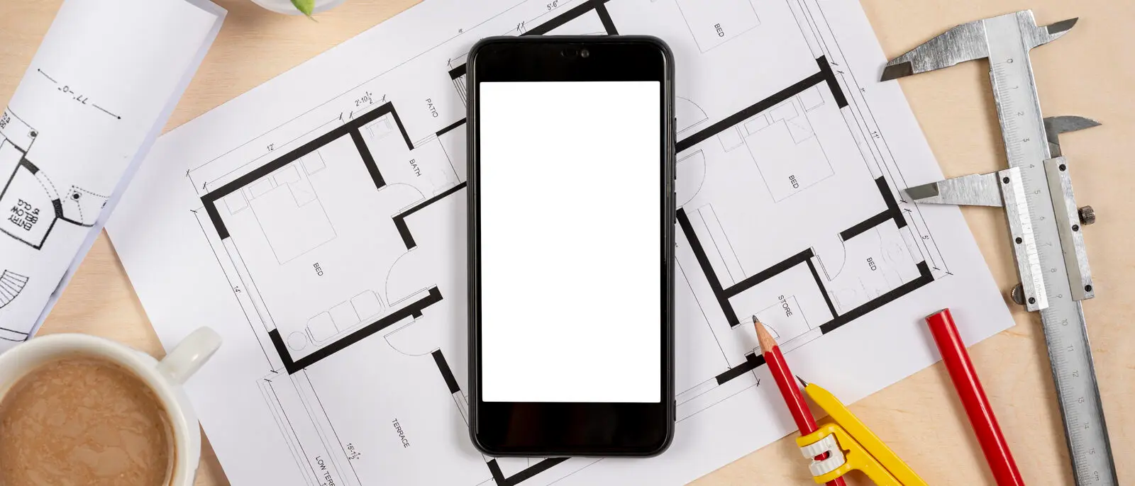 A smartphone resting on architectural plans with measuring tools, representing how a clear app specification determines development cost