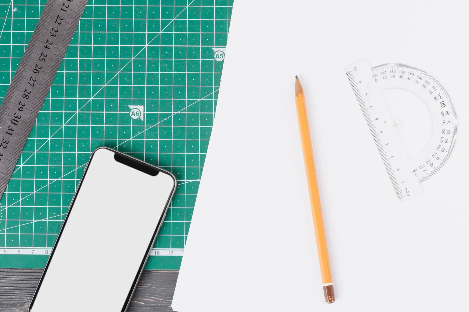 A phone beside a protractor, ruler and pencil on a cutting mat, representing the measurable scope decisions that determine app development cost