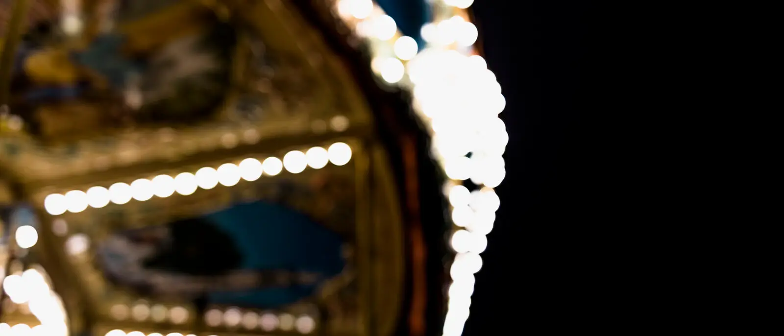 A softly blurred illuminated carousel against a black night sky, evoking the atmosphere of a carefully built themed environment