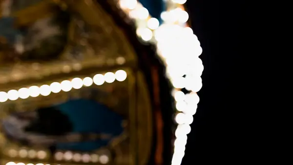 A softly blurred illuminated carousel against a black night sky, evoking the atmosphere of a carefully built themed environment