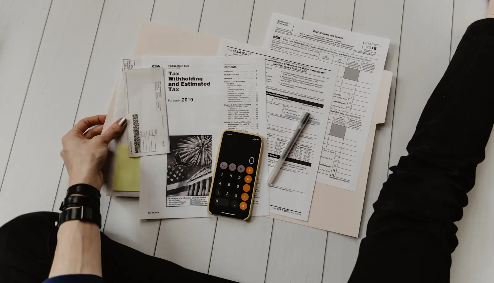 Tax forms and schedules spread across a desk, being sorted by hand