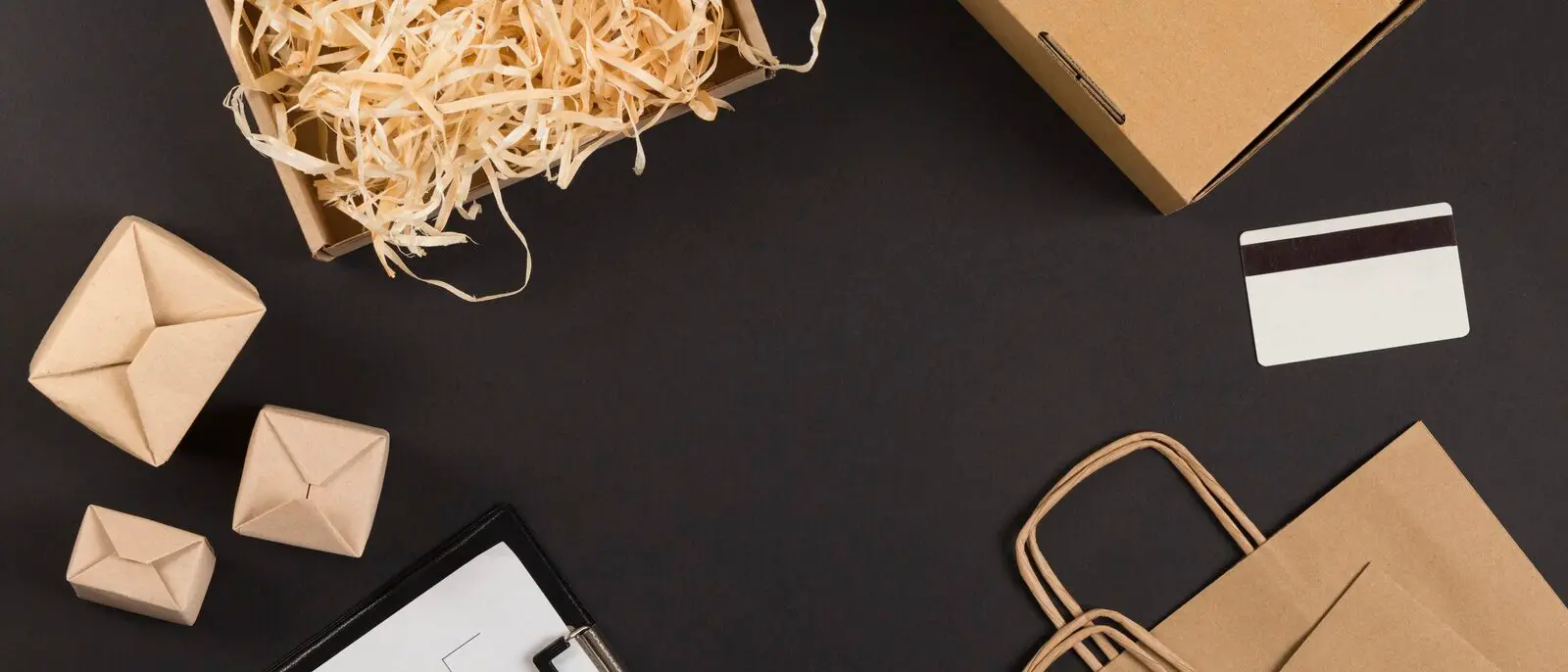 Ecommerce packaging, kraft boxes, shipping bags and an order form arranged on a dark surface, representing the fulfillment side of a small online store