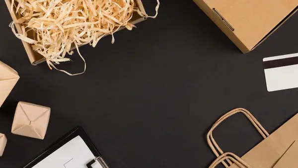 Ecommerce packaging, kraft boxes, shipping bags and an order form arranged on a dark surface, representing the fulfillment side of a small online store