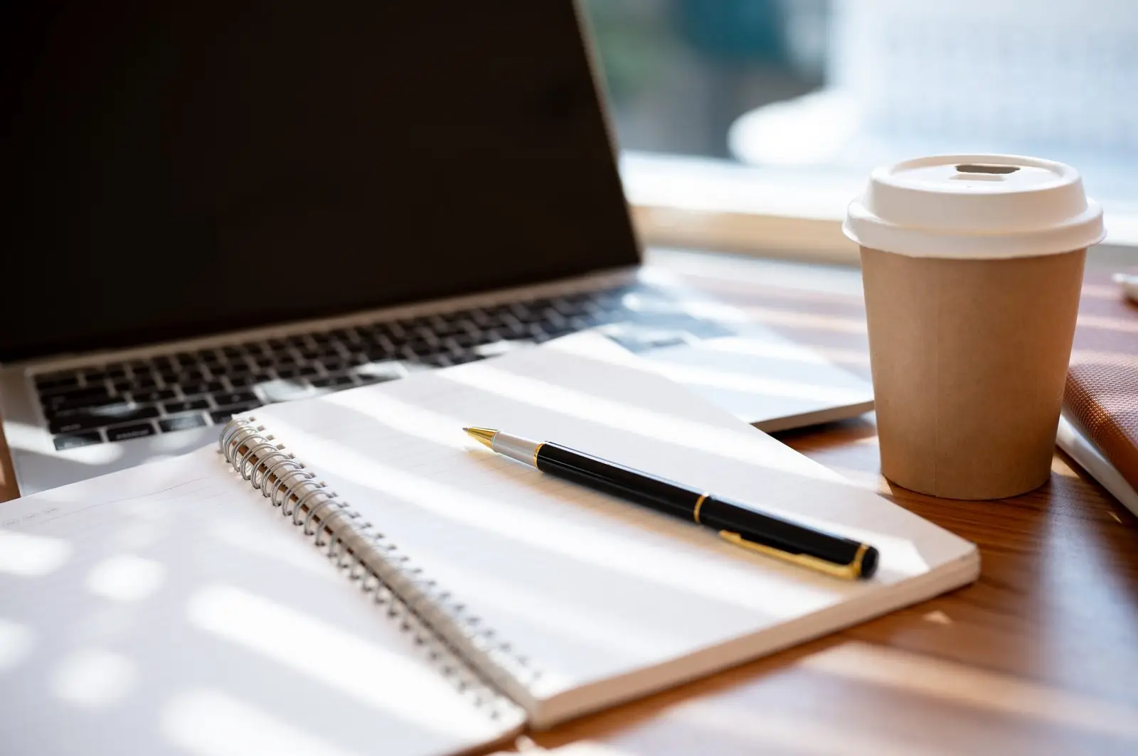 Laptop, open notebook, pen, and coffee on a wooden table representing business technology planning and AI advisory work